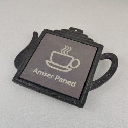 Welsh Heather Blue Square Slate and Black Iron Teapot Stand, with Laser engraved image of Cup and saucer with text reading 'Amser Paned', (Welsh for 'Tea Time'). Made by Inigo Jones Slate Works.
